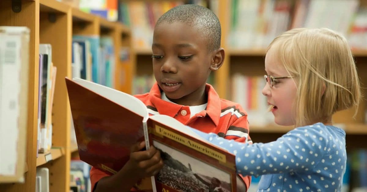 Two schoolchildren reading a book together in a library, representing student support and school nursing
