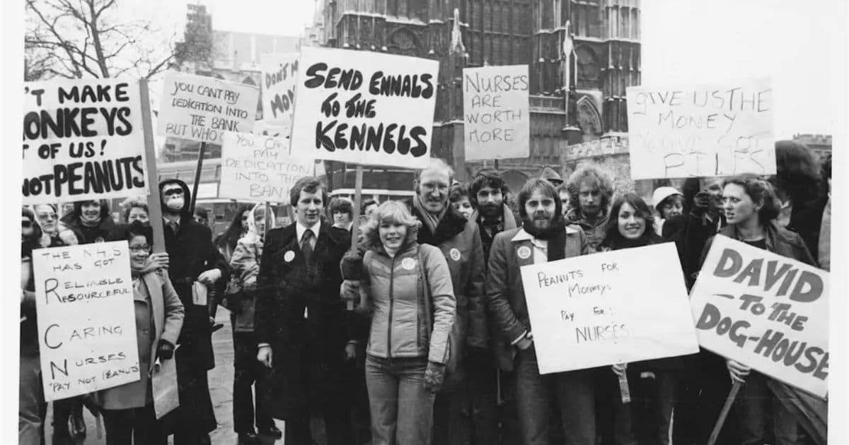 Black-and-white photograph of the RCN Pay Not Peanuts campaign in 1979, with nurses and supporters holding protest signs outside a historic London building